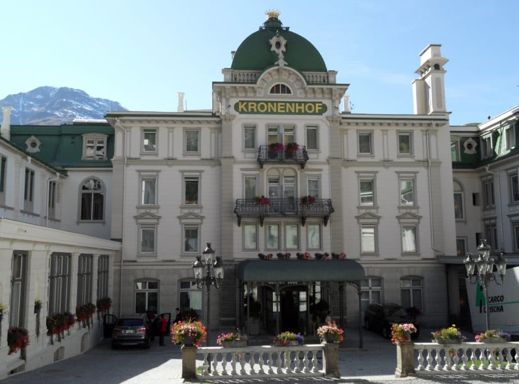 Elegant facade of Grand Hotel Kronenhof with green domed roof and surrounding alpine landscape makes for a luxury Swiss adventure.