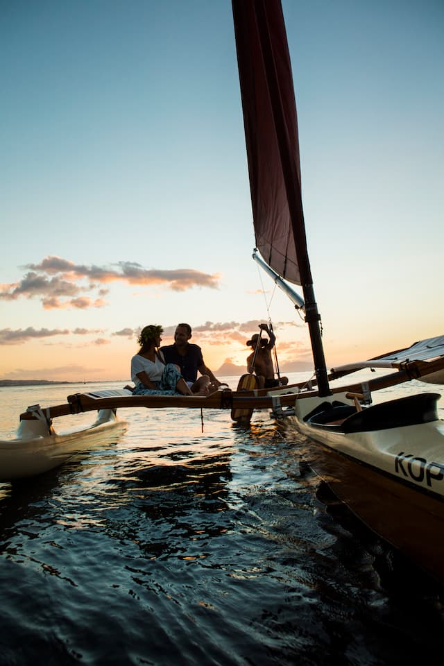 Couple taking a romantic sunset cruise in Tahiti on an outrigger canoe with a Tahitian man paddling.