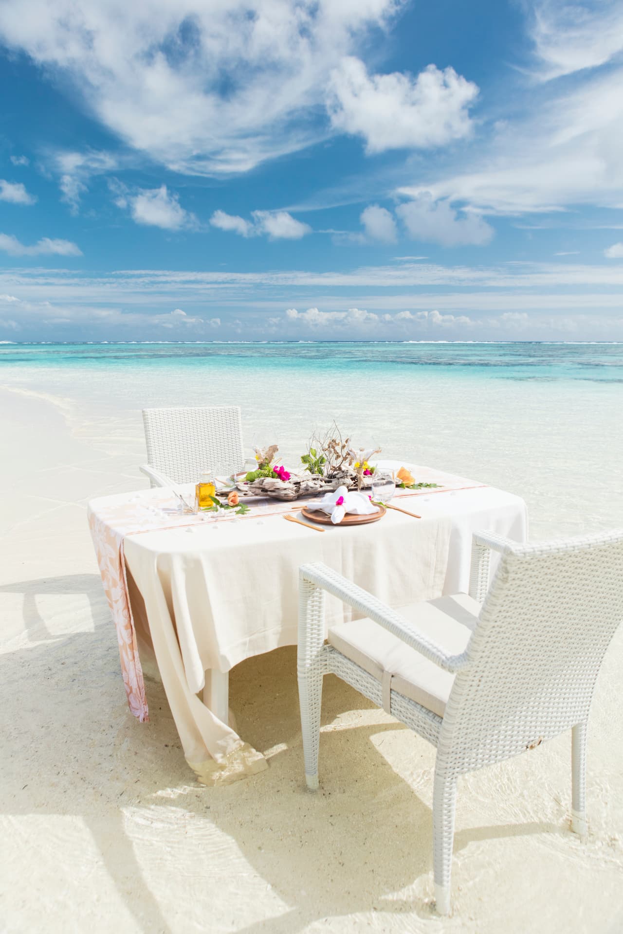 A luxurious picnic setup on a secluded white sand beach with the beautiful ocean in the background and wispy clouds in the sky.