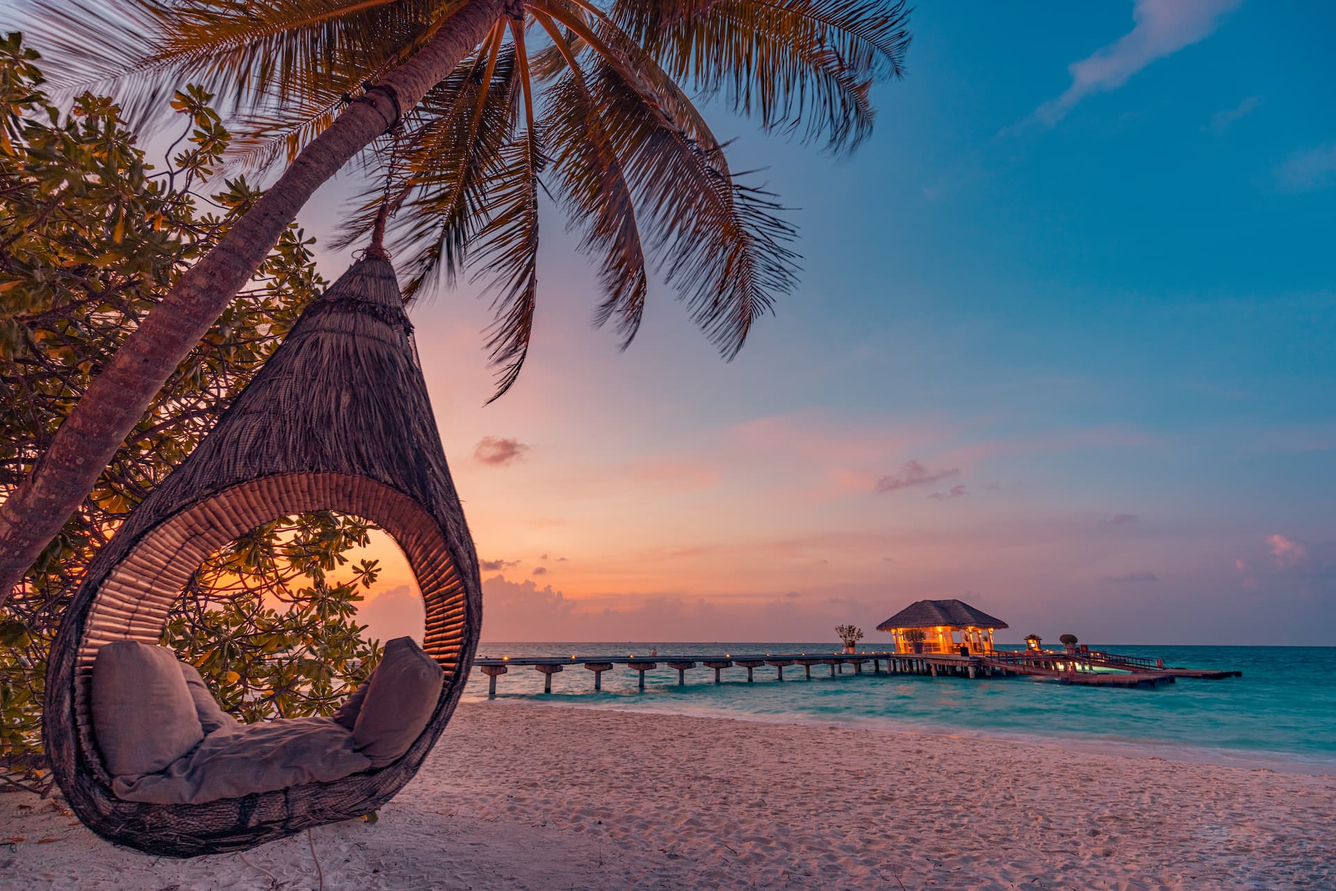 Romantic beach swing with a sunset and pier with overwater bungalow in the background