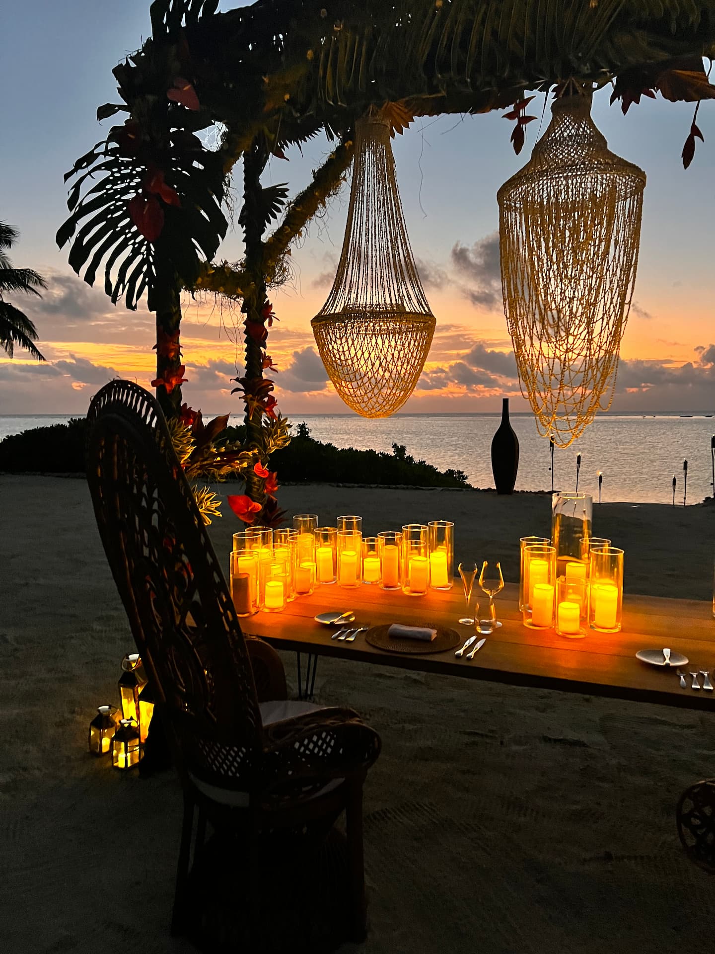 Romantic dinner setup under the stars on the beach with candles casting an orange glow.