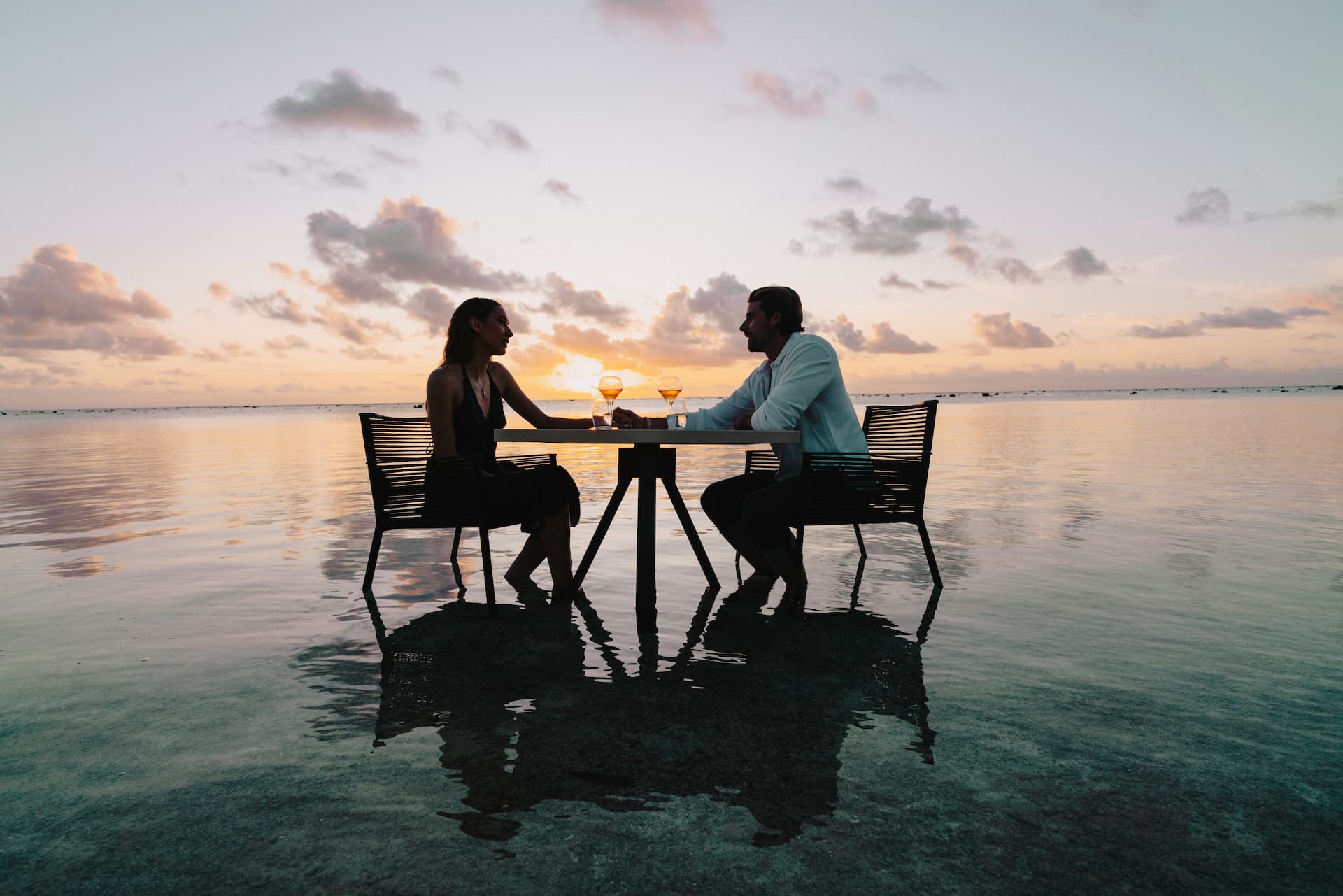 Couple enjoying a romantic sunset dinner on the beach at The Brando Resort.