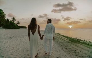 Couple walking hand-in-hand on the beach at sunset.