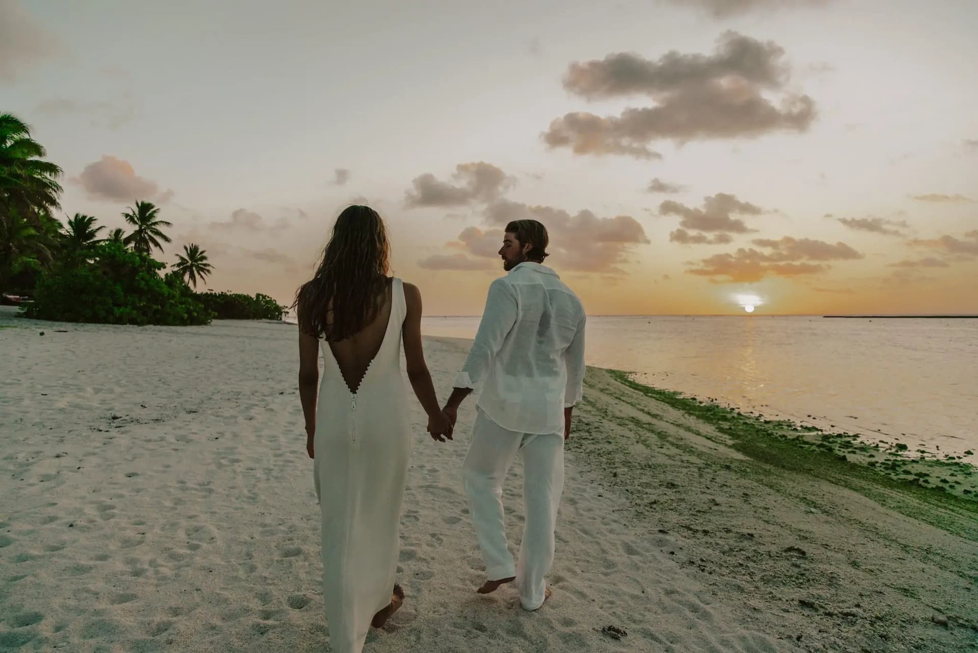 Couple walking hand-in-hand on the beach at sunset.