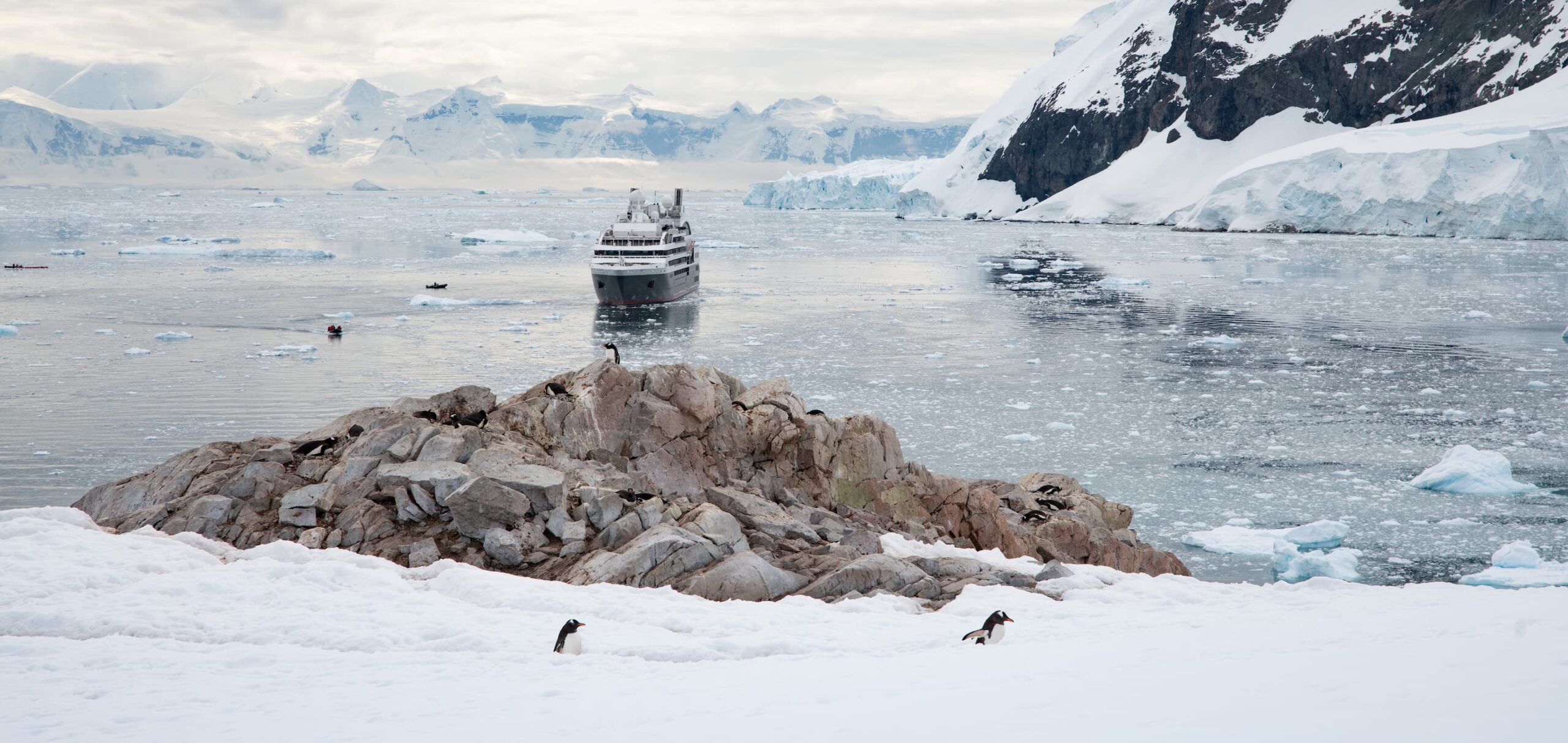 Ponant Le Boréal navigating through icy waters with snow-capped mountains and Adele penguins on Antarctica luxury journey.