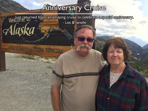 A couple standing on a beach in front of a "Welcome to Alaska, the Gateway to the Klondike" sign during their anniversary cruise.