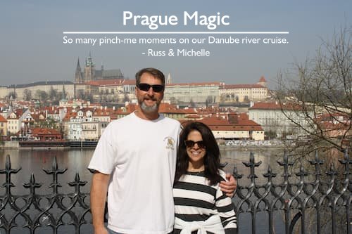 Couple in Prague standing by the river with Prague Castle in the background, enjoying a river cruise vacation filled with pinch-me moments, planned by Sheila Cannon.