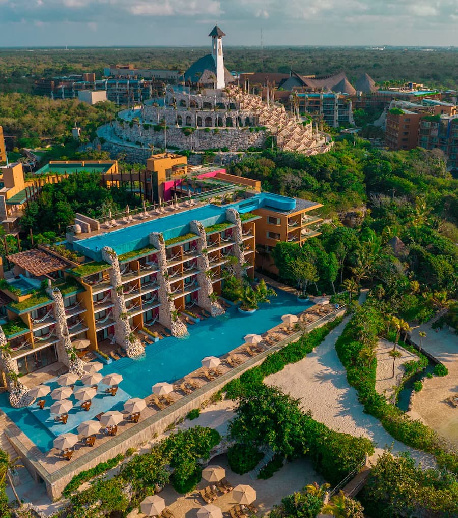 Aerial view of Hotel Xcaret Mexico with oceanfront suites and church in the background.