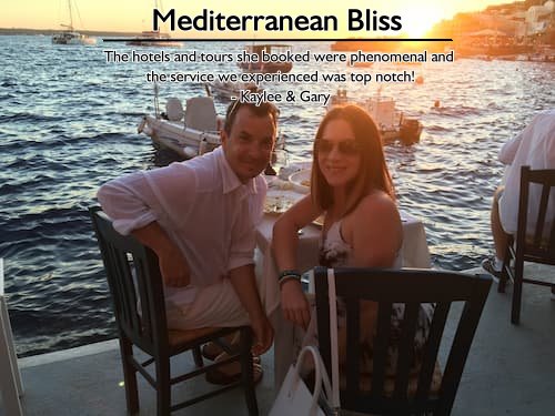 Smiling couple dining oceanside in Santorini with boats bobbing at anchor on the Mediterranean Sea, showcasing Sheila’s incredible honeymoon planning.