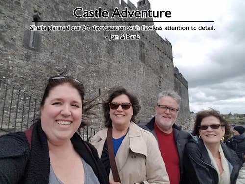 Four smiling travelers standing in front of a castle in Scotland during their flawless 34-day British Isles vacation planned by Sheila.